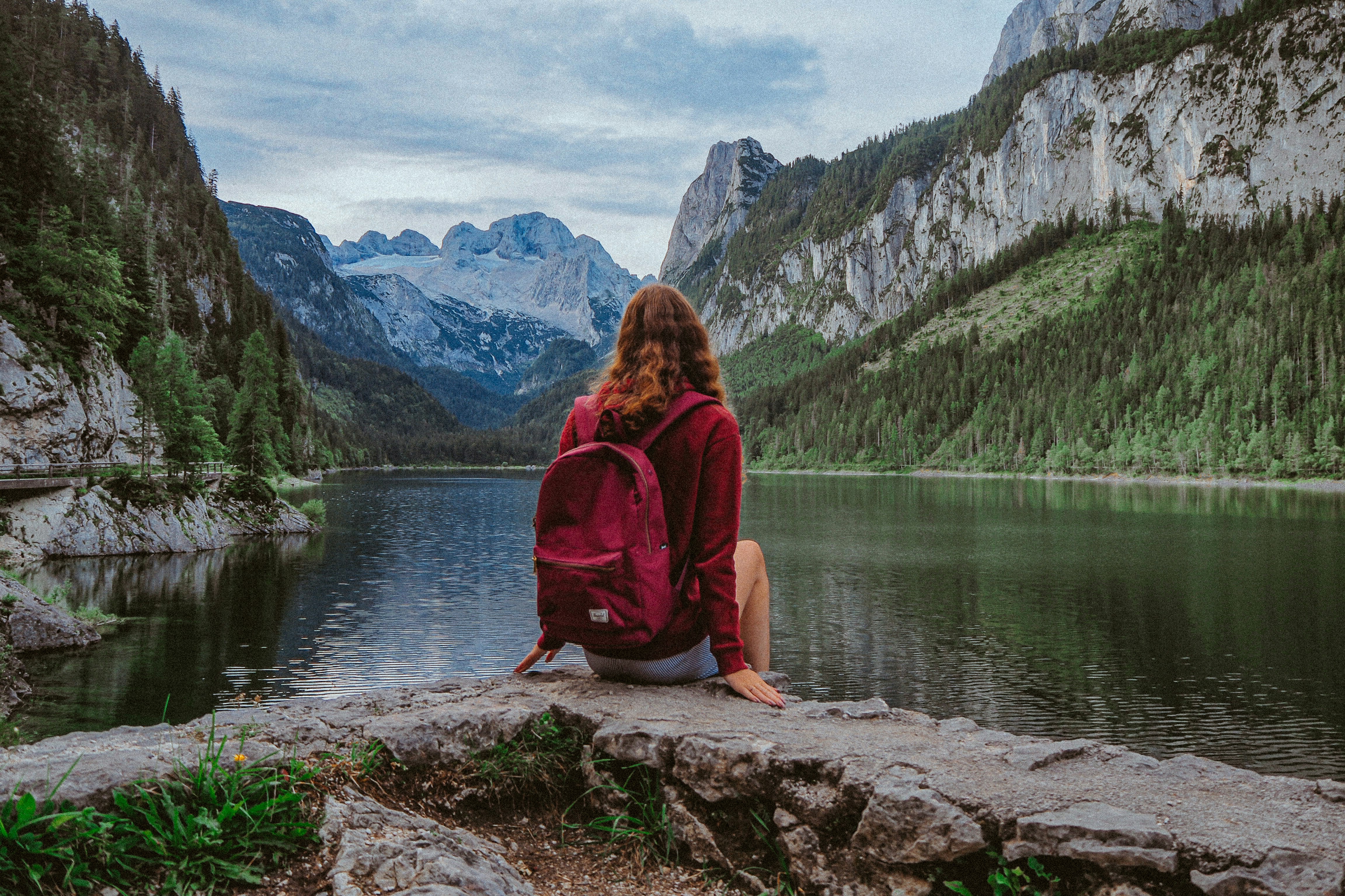 woman in red hoodie sitting on rock near lake during daytime